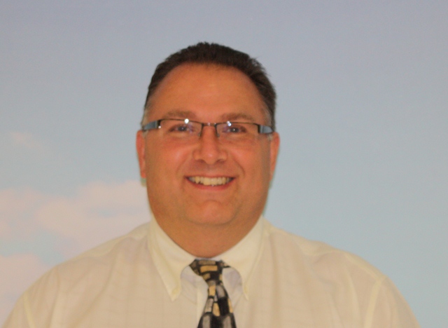 Gary, Director of Motability Enterprises Limited smiling to camera. He is wearing glasses with silver frames, a white shirt and a patterned tie in black, grey and yellow.